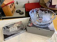 Photo showing a clear glass serving bowl and a rectangular serving platter, both with etched floral designs and scalloped edges, placed on boxes.
