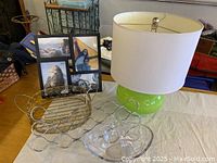 Full view of the lot showing a green ceramic lamp with white shade, black multi-photo frame, decorative gold-toned scarf hanger, and a clear glass bowl.