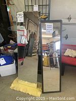 Two tall rectangular framed mirrors standing upright, reflecting a cluttered background