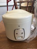 White rice cooker with closed lid and front control panel with indicator lights and switch button, placed on a wooden surface.