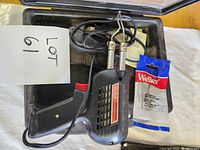 Photo of Weller soldering gun inside its black molded plastic case with a power cord and a sealed pack of soldering tips.