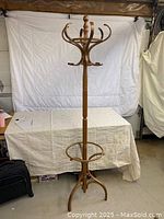 Full view of wooden swivel coat rack showing multiple hooks, circular support ring, and tripod base design in a room setting.