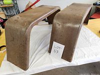 Photo shows two large rusted metal trailer fenders on a table with a small 'Lot 67' card between them.