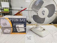 Image shows a boxed Campbell Hausfeld exhaust fan next to an assembled white Hampton Bay table fan with three black blades and control dials.