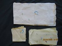 Top view of folded small white tablecloth showing floral embroidery, stacked with folded yellow napkins embroidered with flowers and animals