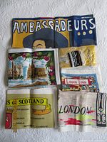 Top view of 5 vintage linen tea towels with UK themed prints and sealed yellow plastic tablecloth