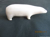 Side view of a smooth, light-colored vintage Inuit polar bear carving, showing elongated body, legs, and head with eye detail.