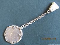 Full view of the key chain against a dark fabric background, showing the chain and coin pendant with its twisted frame.