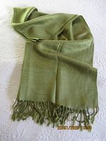 Large green pashmina scarf spread on a white textured surface showing full length and fringe detail.