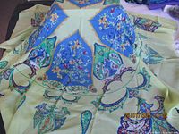 Photo of the scarf spread out showing the intricate blue and green ornate patterns on a beige background.