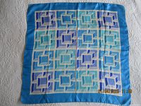Full view of the square blue silk scarf with geometric pattern and blue border laid flat on a surface.