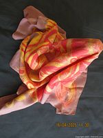 Scarf laid out showing the colorful abstract pattern with dominant orange, red, and yellow hues on brown background.