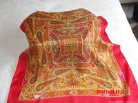 Silk scarf laid out on white surface showing the full square patterned design with warm colors and red border.
