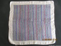 Full view of a small silk scarf with vertical multi-colored patterns and cream border laid flat to show overall condition and design