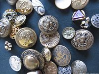 Top view of assorted metal buttons showing various crests and emblems including Canadian and military style.
