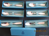 Six vintage silver Birks spoons with Christmas themed engravings displayed in individual blue presentation boxes on a black surface.