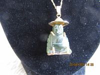 Close-up of the carved jade pendant showing seated figure with hat and gold-tone framing on black background