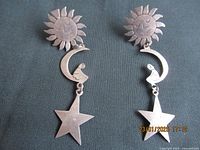 Pair of vintage sterling silver dangly earrings with sun, crescent moon, and star motifs on dark fabric background.