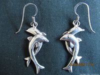Pair of sterling silver earrings in dolphin shapes with French hook attachments laid flat on fabric background, showing front side details.