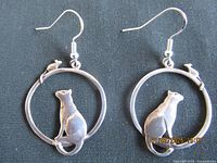 Both earrings displayed showing the cat figure sitting inside the circular frame and the mouse figure perched on top.