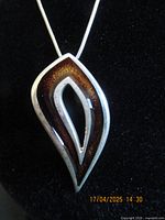 Close-up image of the pendant showing its modern layered teardrop design with dark inlay on silver frame on black background.