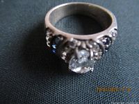 Close-up of sterling silver ring front showing large clear pear-shaped stone and side accent stones on black cloth background.