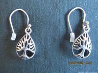 Front view of the earrings showing the teardrop shape and Tree of Life motif on a black background.