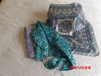 Three blue scarves displayed on neutral fabric background, showing pattern and colors.