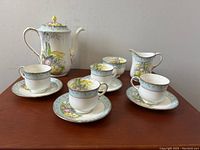 Full view of eleven-piece Aynsley England porcelain coffee set with floral decoration and gold accents on wooden table