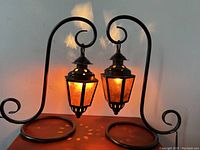 Pair of ambient table lamps with curved metal bases and amber mica shades illuminated, showing warm glow and decorative light patterns.