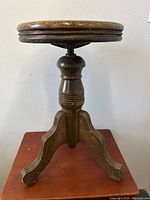 Front view showing the entire adjustable piano stool with three curved legs and turned center spindle.