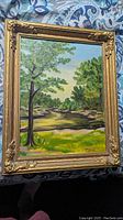 Framed landscape oil painting on board, signed M V Swash, displayed on a fabric background.