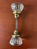 Top view showing two clear crystal glass door knobs attached to brass mounts and threaded shaft on a wooden surface.