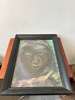 Frontal view of framed pastel painting showing full image and frame details on reddish wood surface.