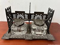Front view of cast-iron double inkwell desk set with two glass inkwells and decorative cast-iron frame.