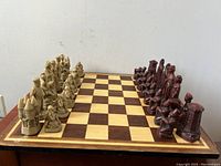 Full chess board with both full sets of cream and maroon figural Napoleonic chess pieces set up for play. Board wooden with inlaid 16x16 squares and decorative border.