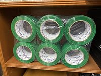 Six rolls of green packing tape shrink-wrapped in plastic viewed from above showing the front side of the rolls.