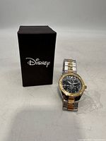 Men's Disney Mickey Mouse watch with black dial and two-tone metal bracelet next to black Disney box