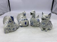 Four animal-shaped ceramic creamers (chicken, turkey, duck, pig) arranged side by side showing front view and detailing of blue floral and butterfly decoration.