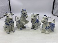 Front view of four ceramic creamers shaped as farm animals: cow, horse, lamb, goat, painted in white with blue floral decorations.