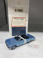 Blue 1963 Chevrolet Impala scale model car with open hood showing engine, labeled with Franklin Mint Precision tag, placed next to original packaging and certificate.