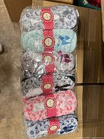 Pack of six pairs of fuzzy slippers in assorted leopard print colors stacked together in plastic packaging