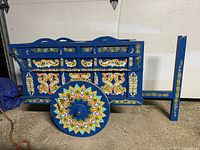 Side view of the blue wooden wagon cart showing intricate floral hand-painted details on wheels and sides.