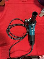 Top view of Makita angle grinder with cord coiled on red surface.
