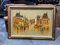 Framed oil on canvas depicting cityscape with buildings and crowd in warm hues, signed.