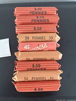 Nine rolls of old pennies in red and brown coin wrappers labeled with quantity and value.