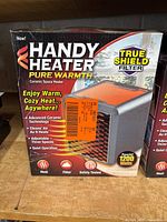 Front view of the cardboard box showing the Handy Heater brand, product image, and highlighted features including 1200 watts power and True Shield filter.