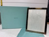 Tiffany & Co. light blue branded box shown next to silver-tone frame with fabric insert inside the frame. Frame stands upright and is clean with minor surface wear.