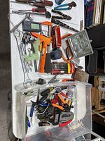 Various miscellaneous tools including hammers, pliers, wrenches, Allen keys, hand lights, measuring tape, and other hand tools on and in a plastic bin.