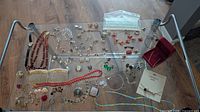 Image of a large assortment of jewelry spread out on a glass table including necklaces, earrings, bracelets, watches, brooches, some with missing stones, and a red jewelry box.